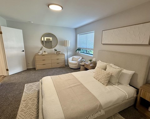 A well-lit bedroom with a large bed and a dresser with a mirror.