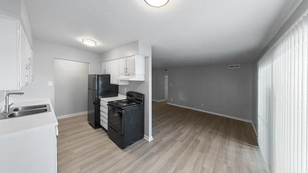 an empty living room with a kitchen with a stove and refrigerator