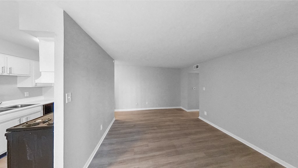 the living room and kitchen of an apartment with grey walls and wood flooring