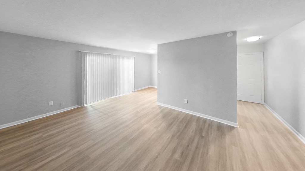 the living room and dining room of an apartment with wood flooring and white walls