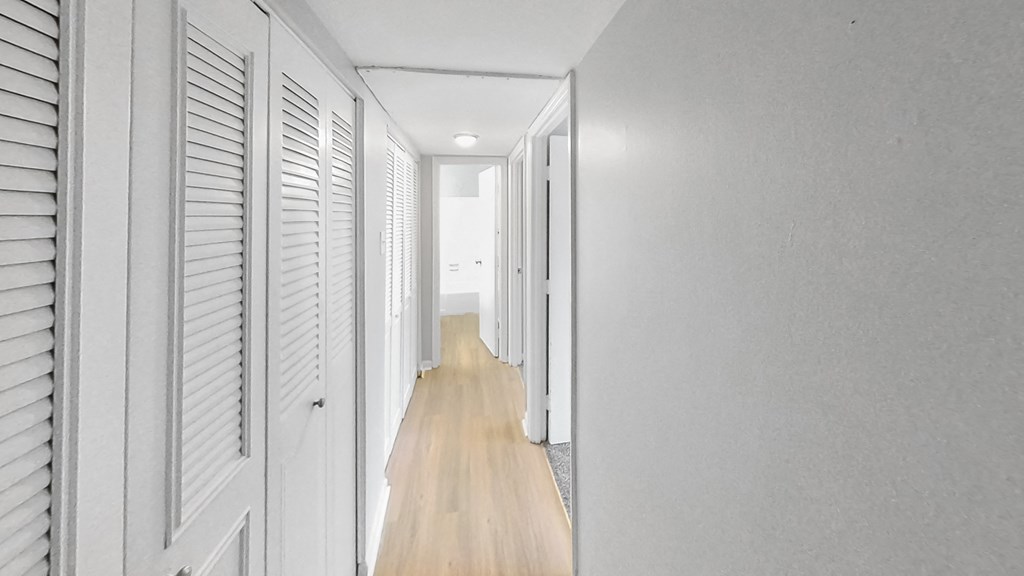 a white hallway with white shutters and a wood floor