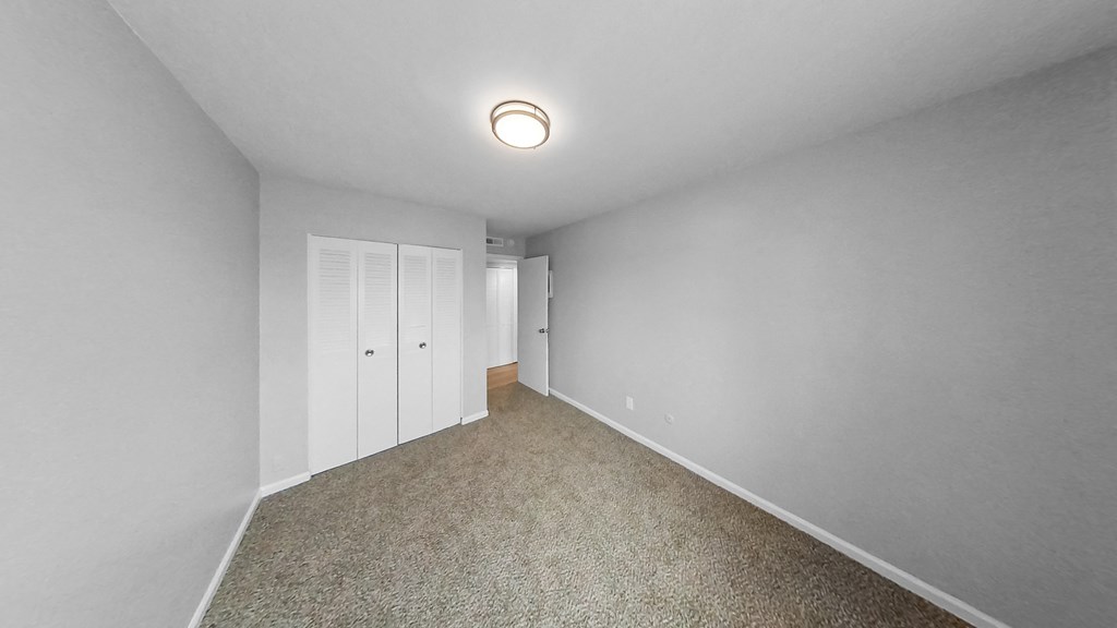 a bedroom with white walls and carpet and white closet doors