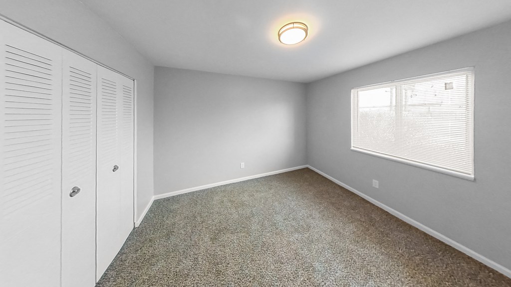 an empty bedroom with a window and a closet