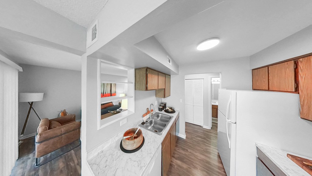 the kitchen and living room of an apartment with white walls and wood flooring