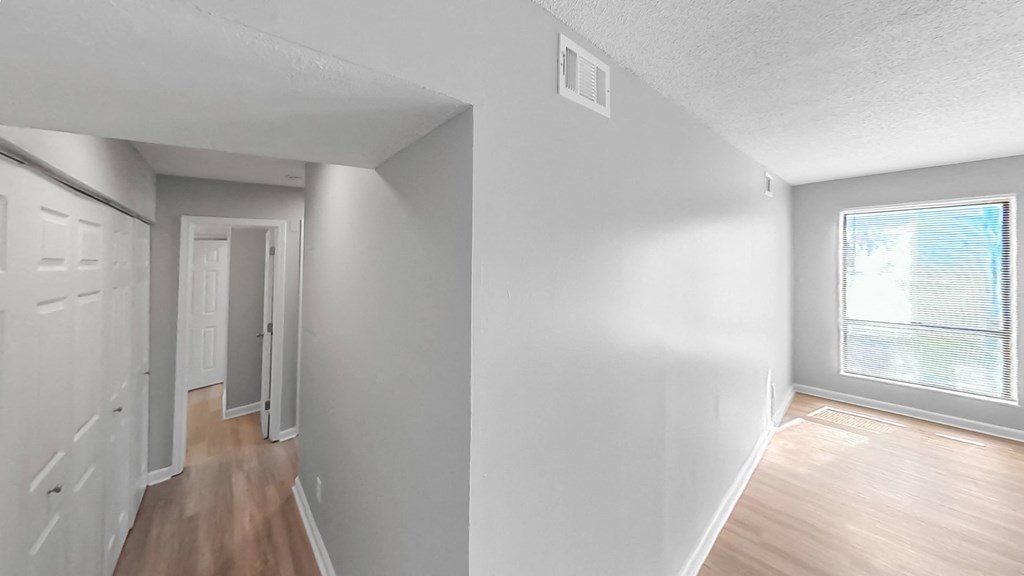 the living room and dining room of an apartment with white walls and wood floors