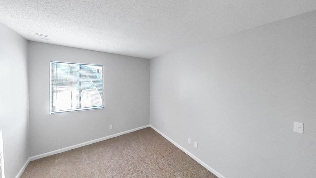 an empty bedroom with a window and carpeting