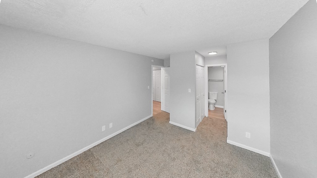 the living room of an apartment with white walls and carpet
