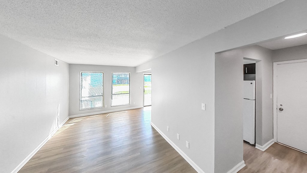 the living room and dining room of an apartment with white walls and wood floors