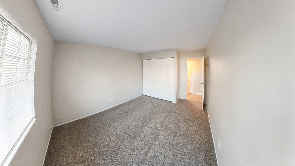 an empty bedroom with a carpeted floor and a door to a closet
