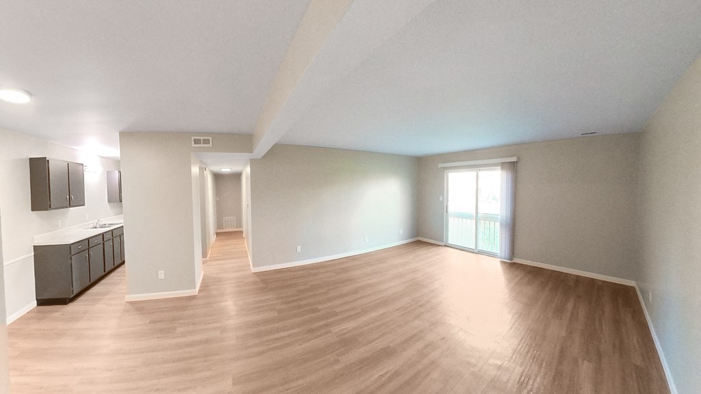 an empty living room with wood flooring and a kitchen