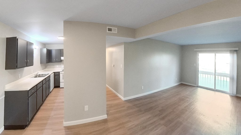 an empty living room and kitchen with wood flooring and a window