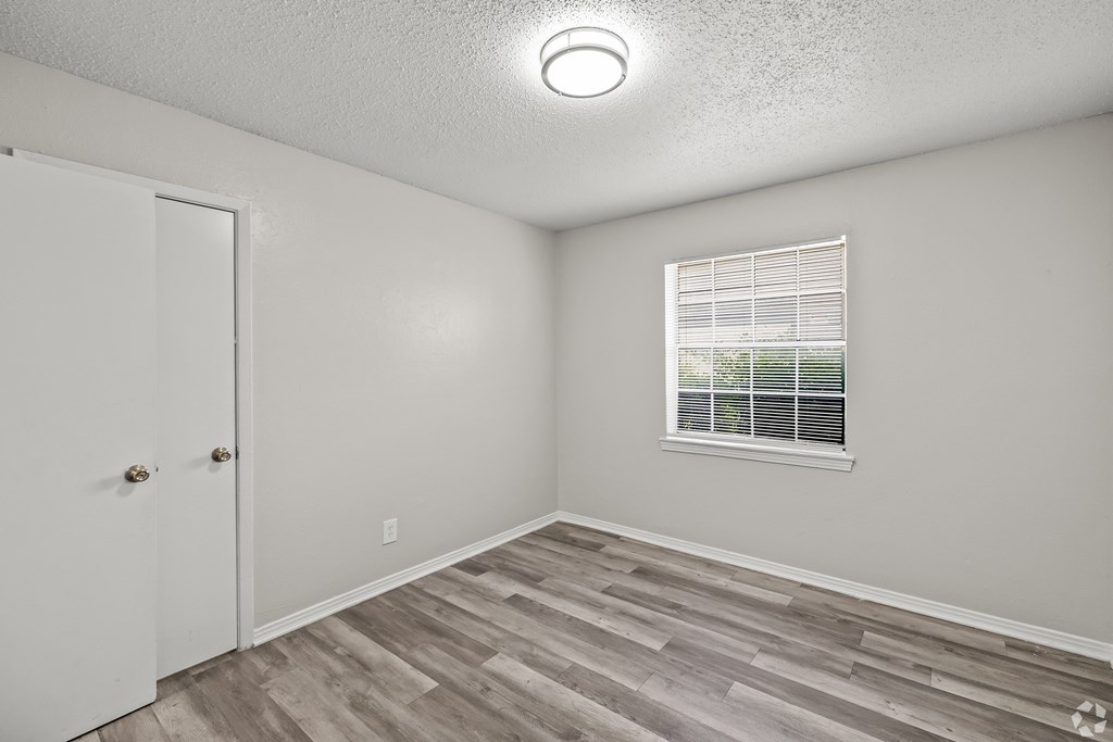 A room with a white door, a window with blinds, and a wooden floor. at La Bella Apartments, Fort Worth, Texas