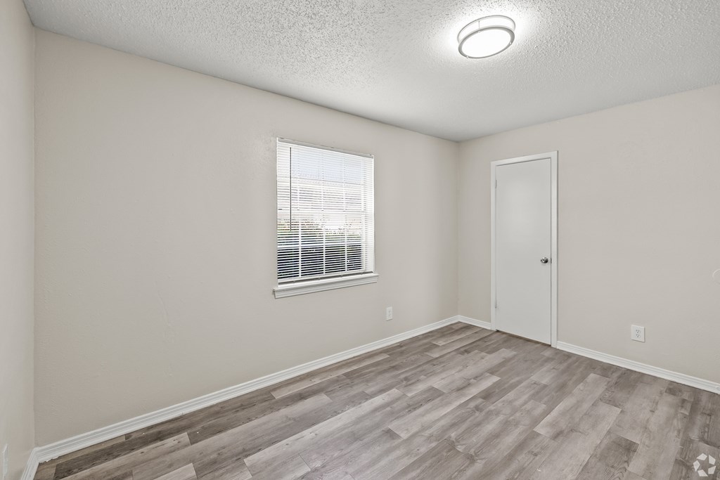 A room with a wooden floor and a window with blinds. at La Bella Apartments, Fort Worth, 76116
