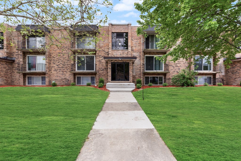 exterior view of a brick apartment building with green grass and a sidewalk