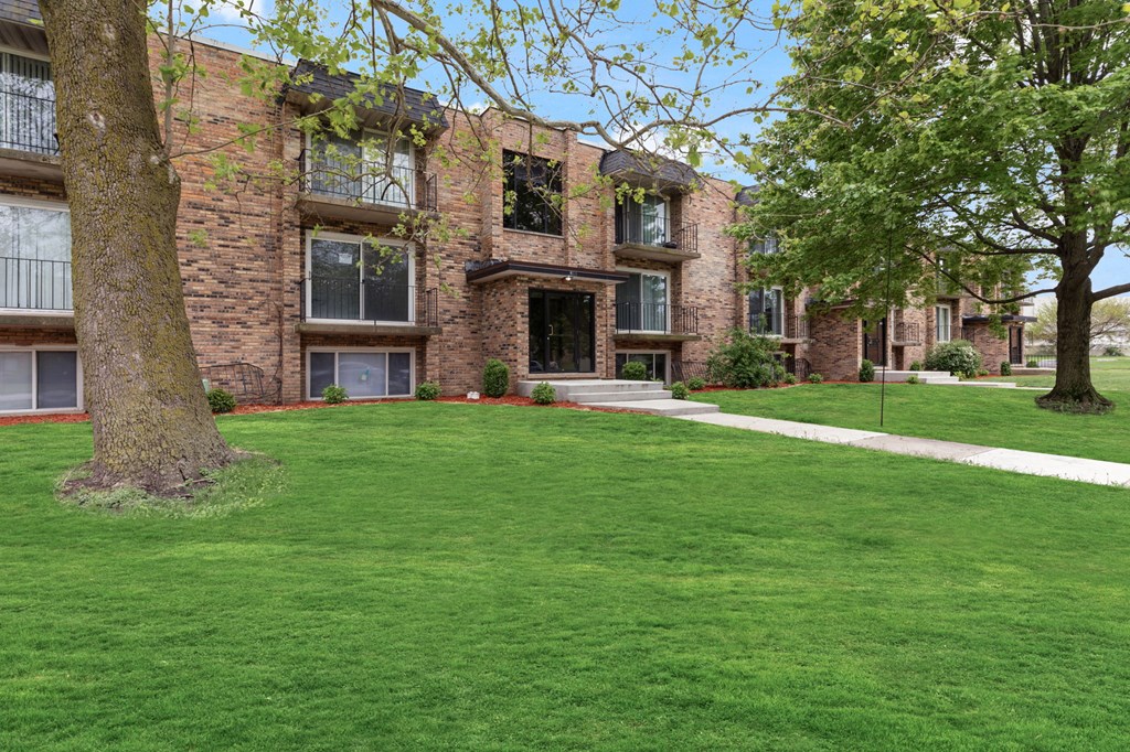 exterior view of a brick apartment building with green grass and trees