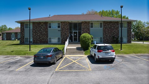 Two cars are parked in a parking lot in front of a brick building.