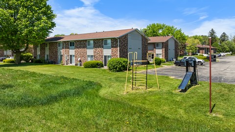 A playground with a slide and a ladder is in front of a building.