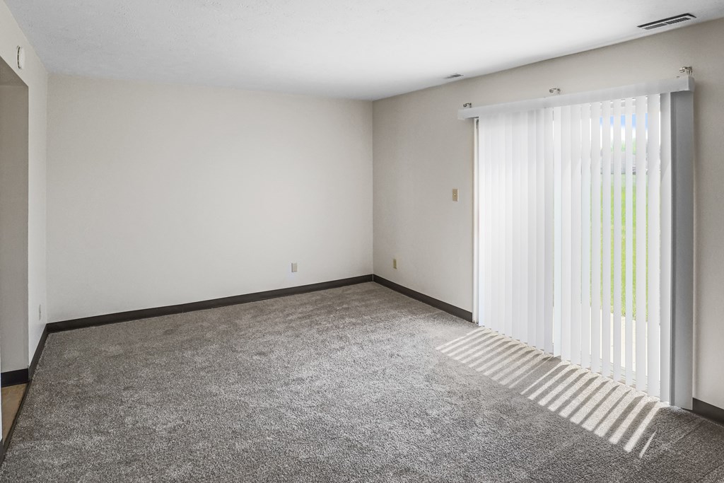 A room with a carpeted floor and a window with blinds.