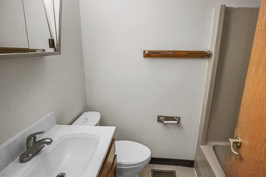 A bathroom with a white sink, toilet, and a wooden door.