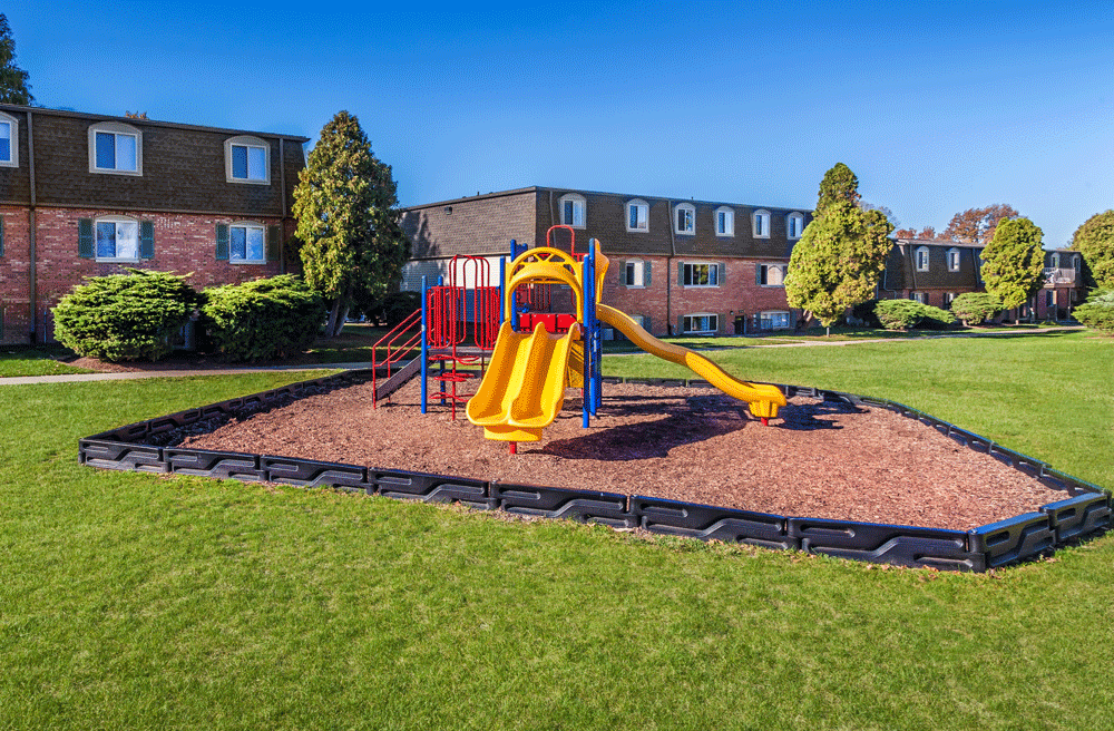 a playground in the middle of a grassy area with a building in the background