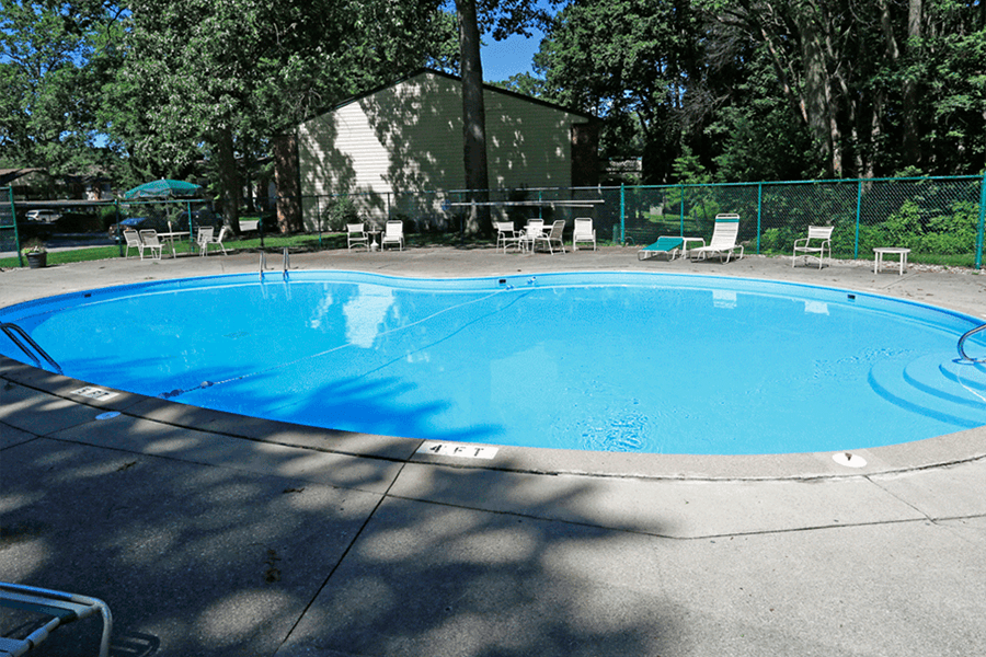 a large swimming pool with a fence around it and a patio with chairs and umbrellas