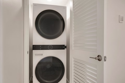 A white door is open to reveal a black washing machine and dryer.