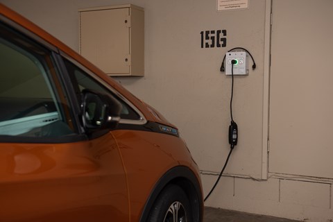 An orange car is plugged into a charging station labeled 156.