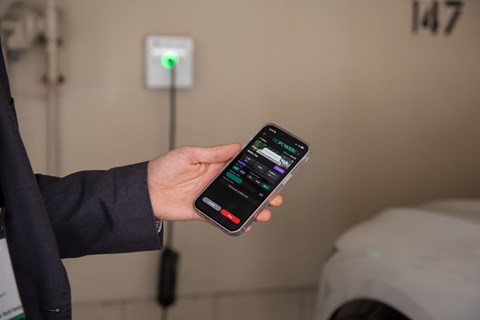 A person holding a smartphone with a charging station in the background.