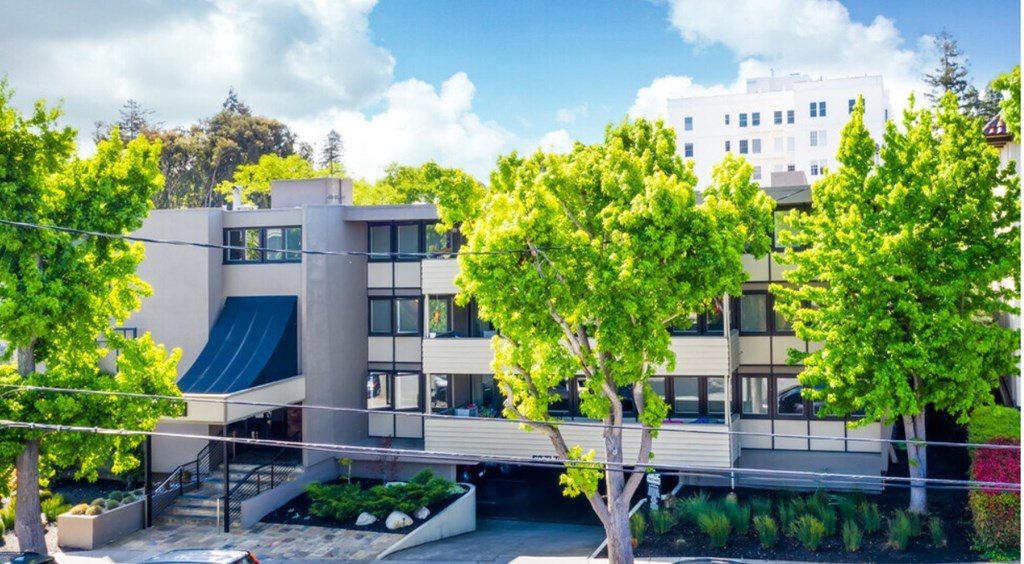 A modern building with a flat roof and large windows is surrounded by trees.