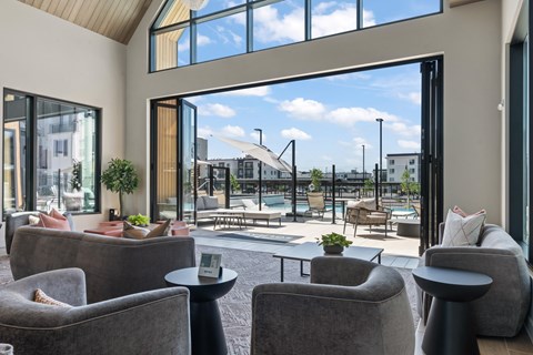 A modern living room with grey couches and a view of a pool and buildings outside.