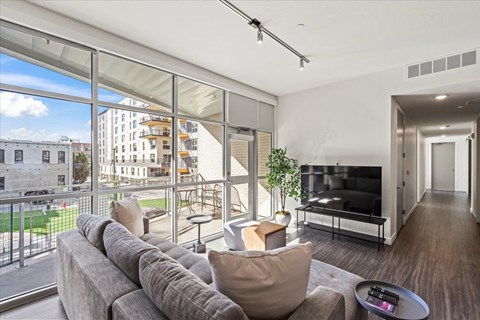 A modern living room with a grey sofa and a large window overlooking a cityscape.