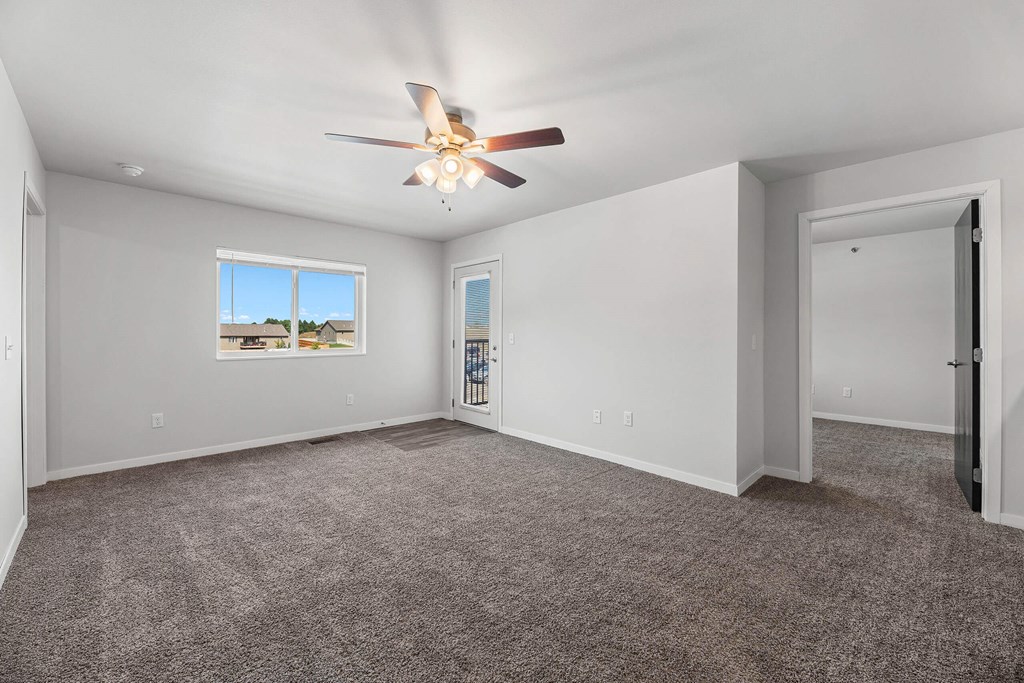 an empty living room with carpet and a ceiling fan at Red Rock Apartments, Rapid City, SD