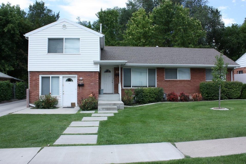 A white house with a grey roof and a red brick wall.