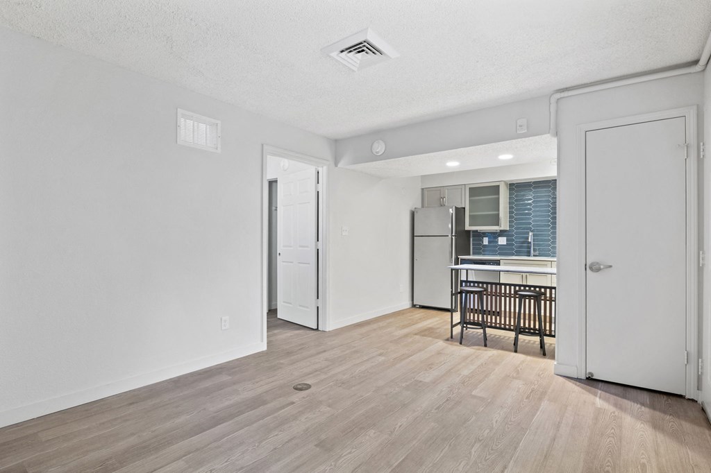 the living room and kitchen of an apartment with a hardwood floor and white walls