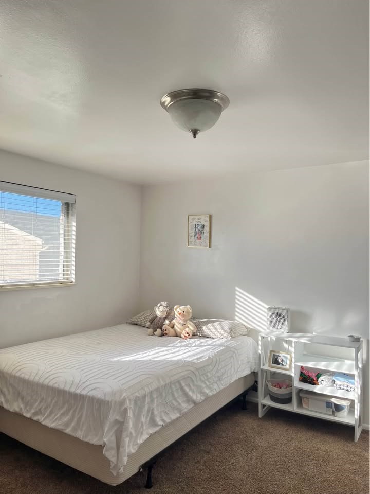 A white bedroom with a bed, nightstand, and a window with blinds.