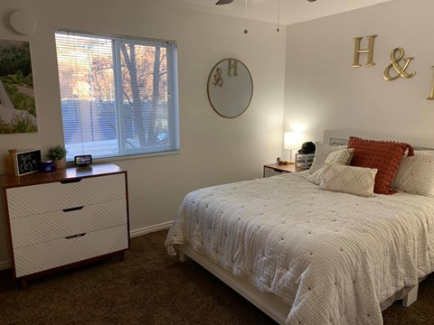 A bedroom with a bed, nightstand, and a window with blinds.