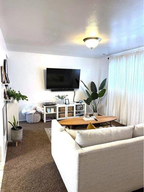 A living room with a white couch and a flat screen TV mounted on the wall.