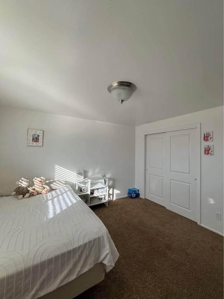 A white bed with a white comforter and a white dresser in a room.