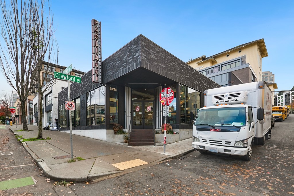 A white truck is parked in front of a building with a black roof.