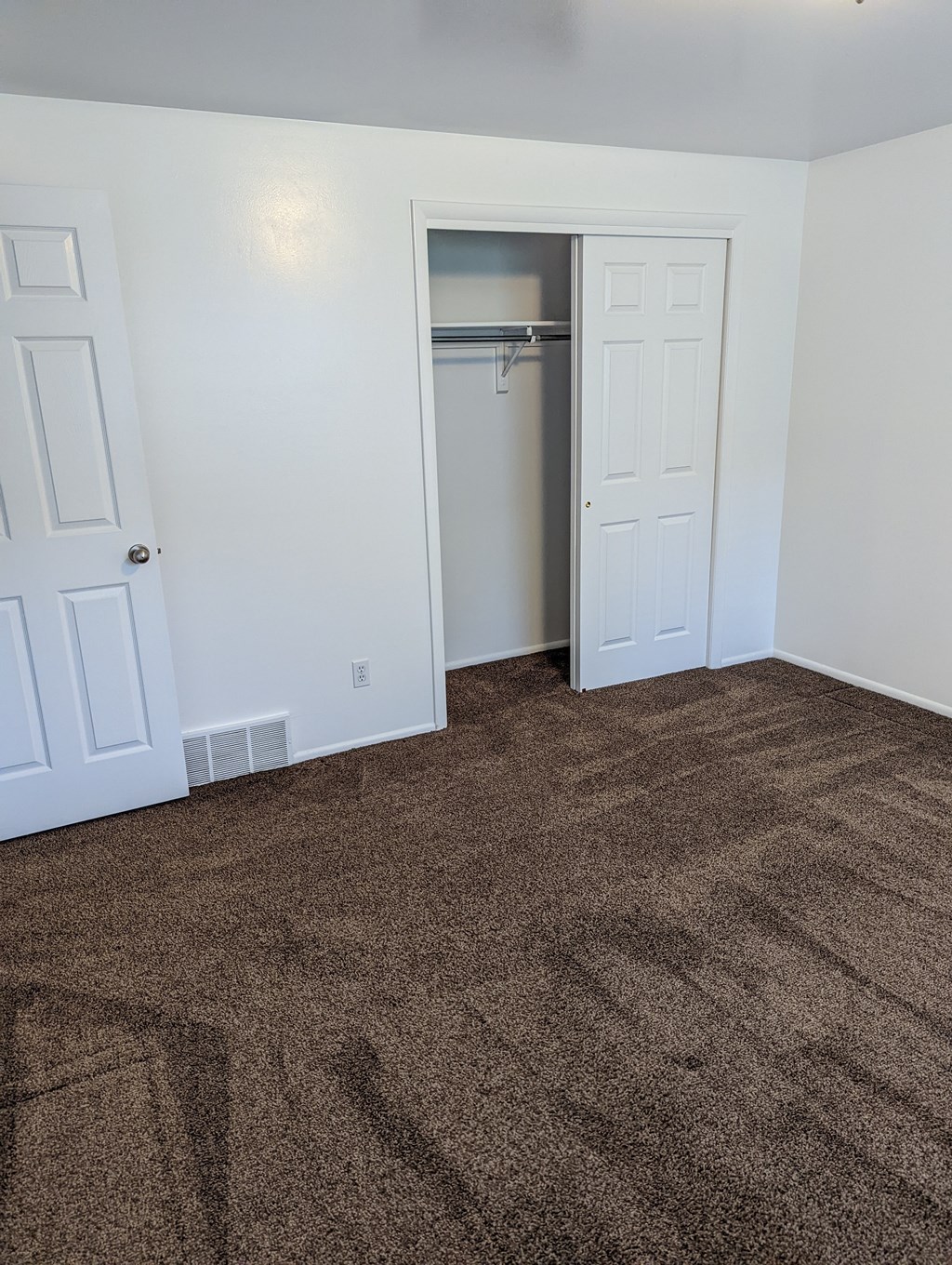 A room with a carpeted floor and a closet with a door open.