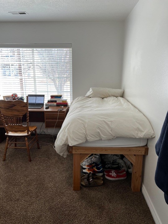 A bedroom with a bed, desk, chair, and shoes.