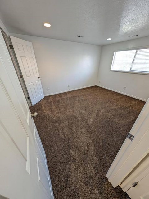A room with a carpeted floor and a window with blinds.