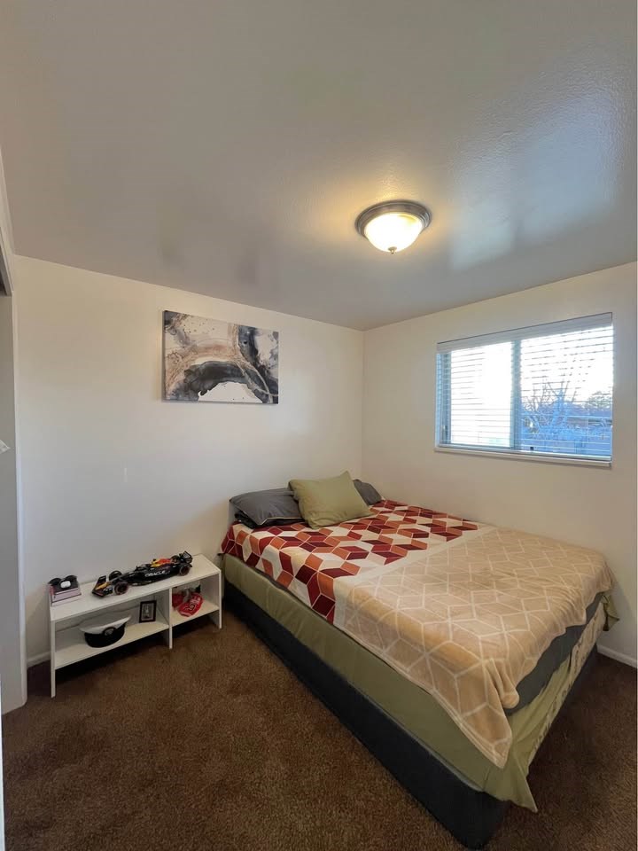 A bedroom with a bed, pillow, and a small table with a remote control on it.
