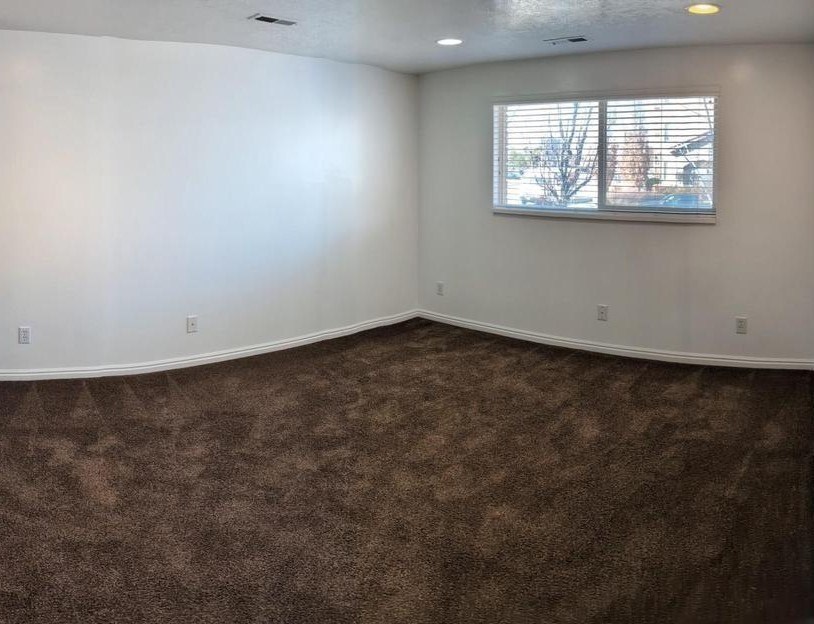 A room with a carpeted floor and a window with blinds.