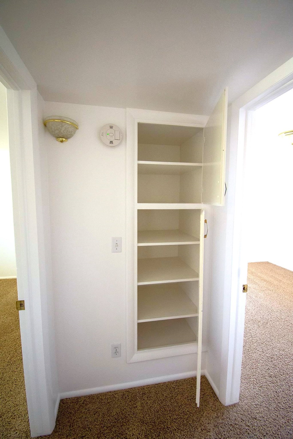 A white closet with a carpeted floor and a light on the wall.