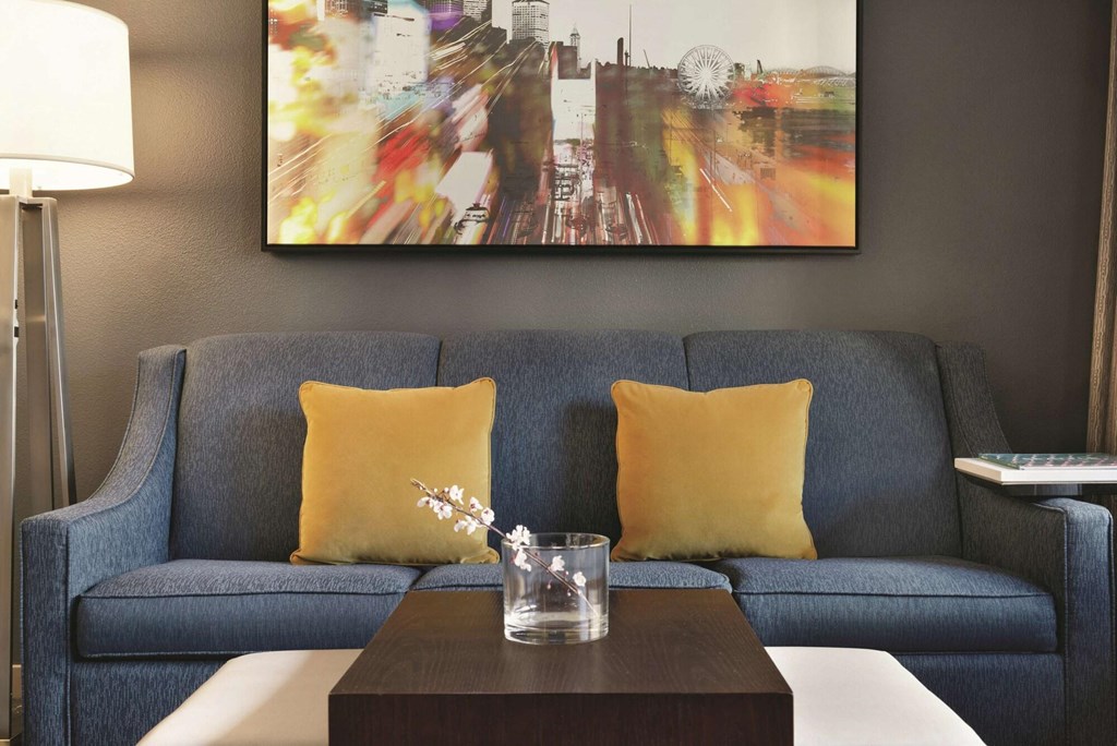 A blue couch with a yellow pillow and a glass of water on a wooden table.at AVIA on Pike Street, Washington, 98101