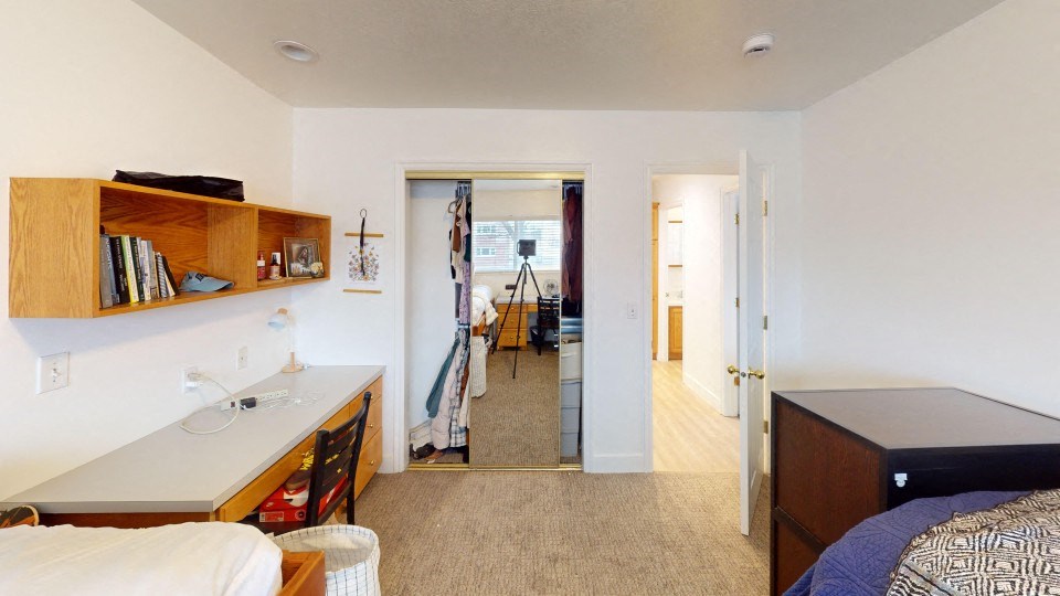 A bedroom with a bed, a desk, and a mirror.