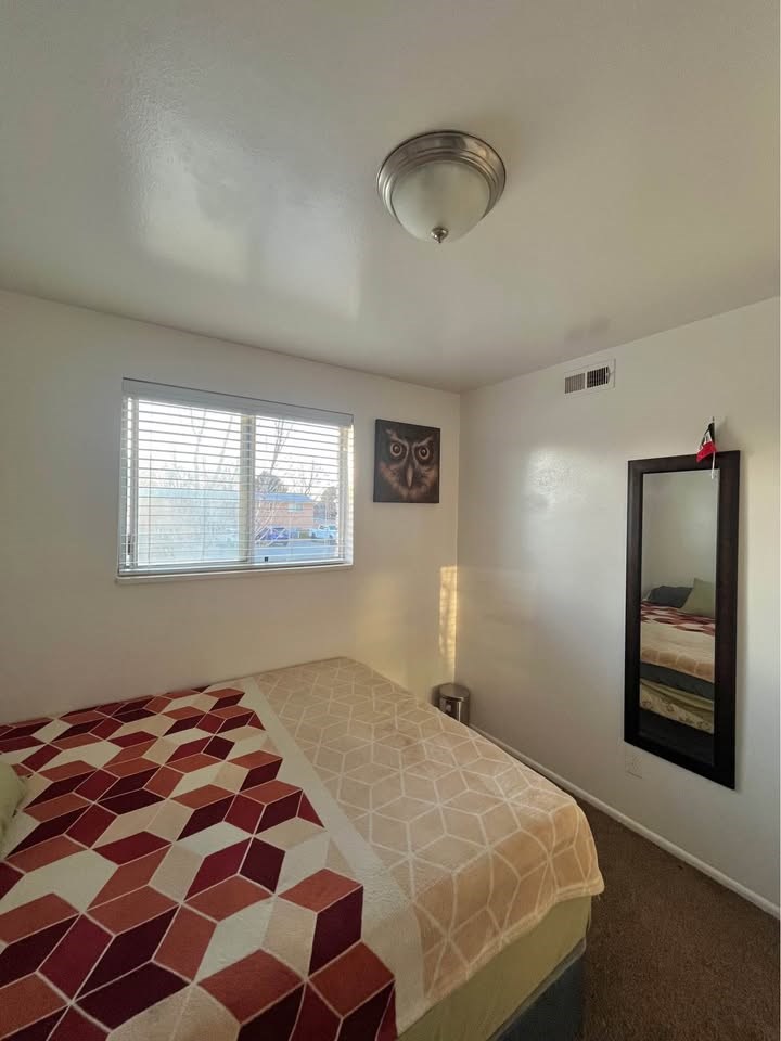 A bedroom with a bed, a mirror, and a window.
