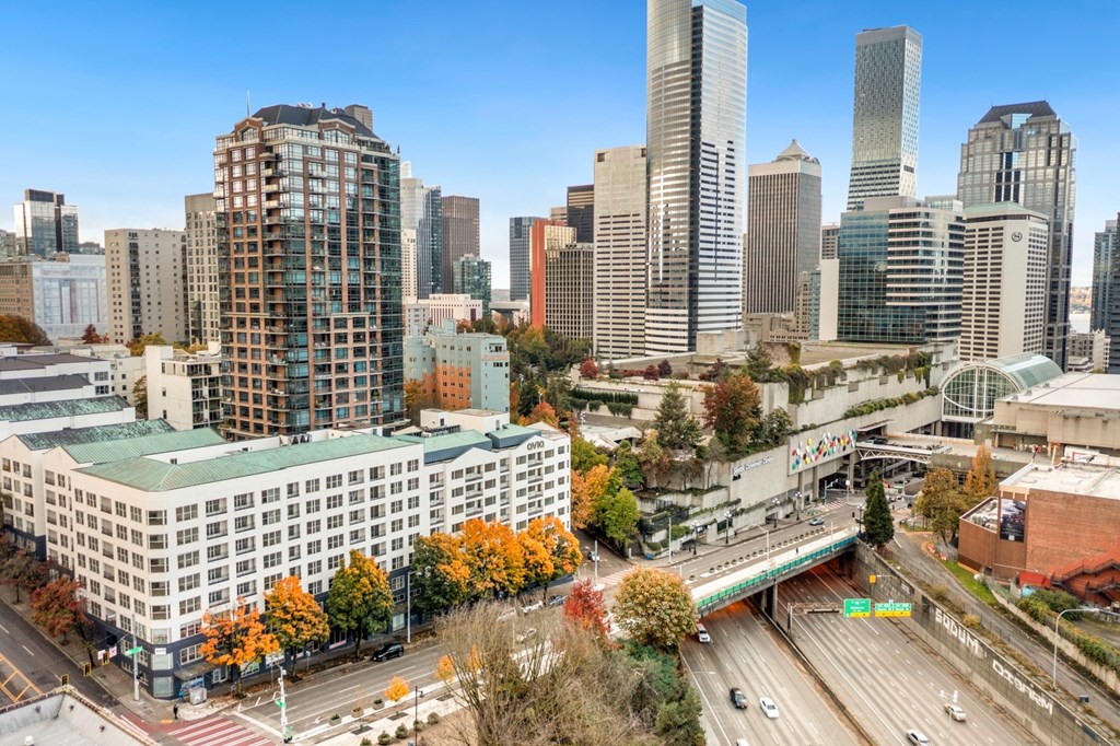 A cityscape with a mix of modern and older buildings, a highway, and autumn trees.