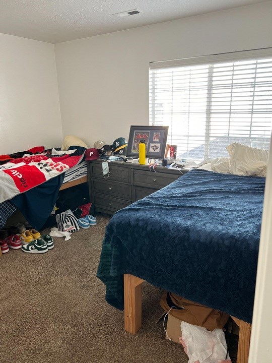 A bedroom with a bed, dresser, and window with blinds.
